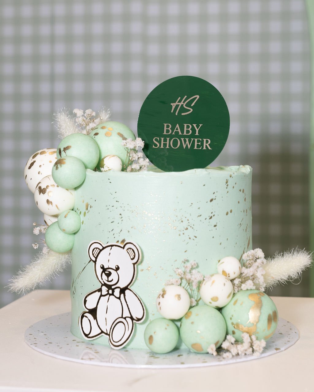 Close-up of the sage green speckled cake with a teddy bear topper and Baby Shower sign