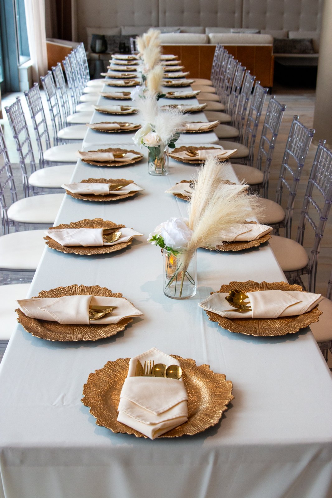 Long banquet table set with gold scalloped chargers, ivory linens, and pampas grass centerpieces