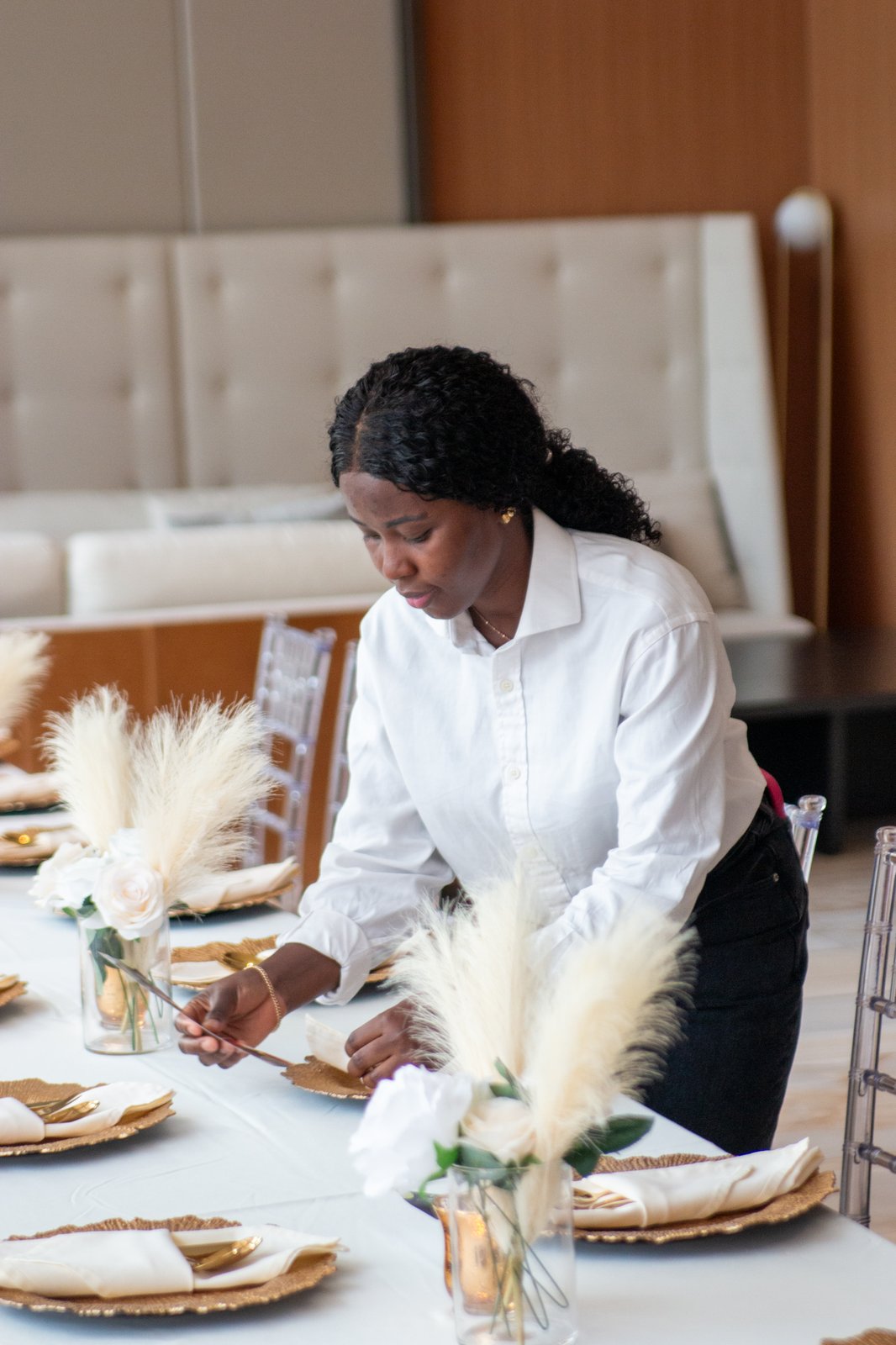 Event stylist putting the finishing touches on a place setting with pampas grass and white roses