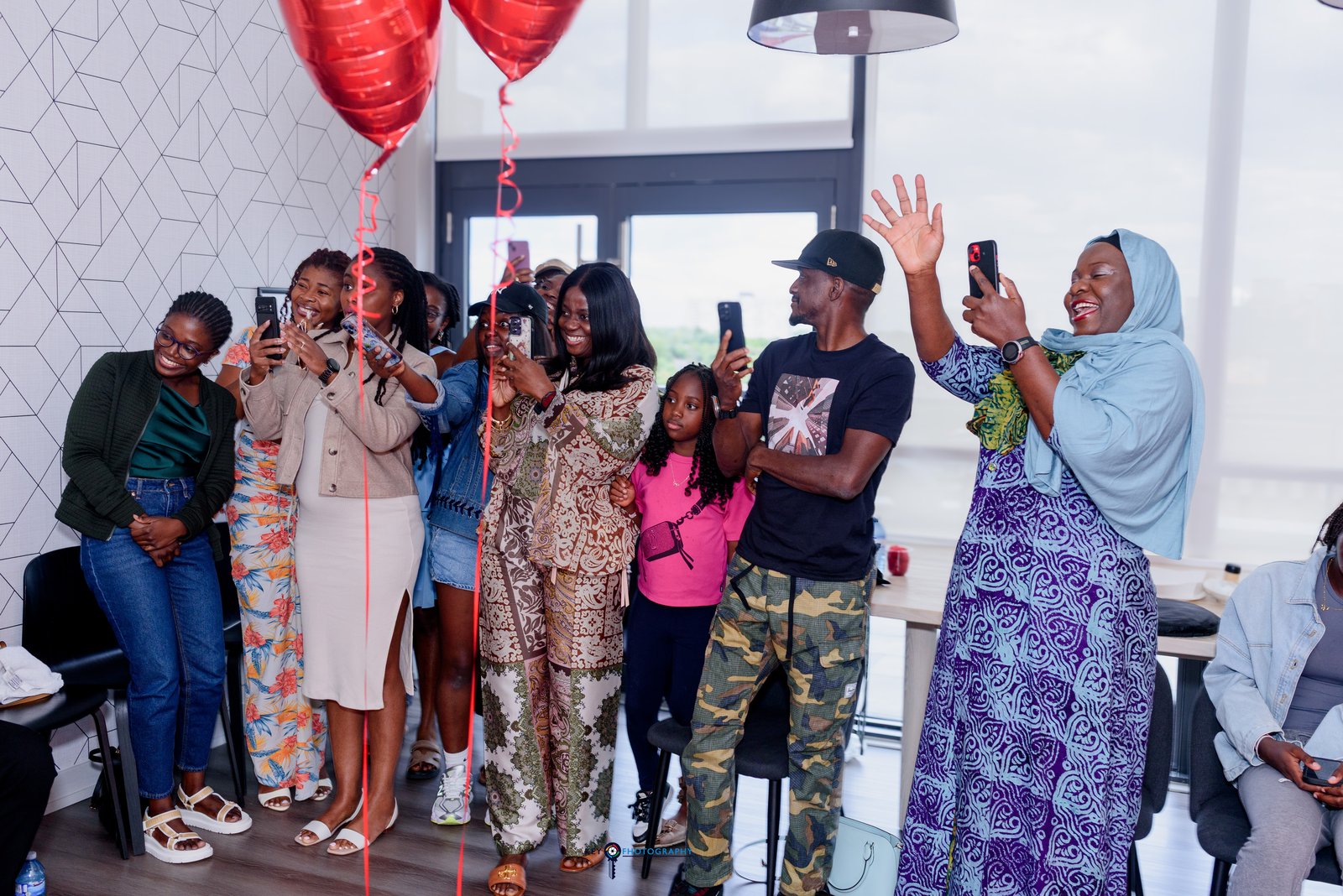 Friends and family filming the moment on their phones, red heart balloons overhead