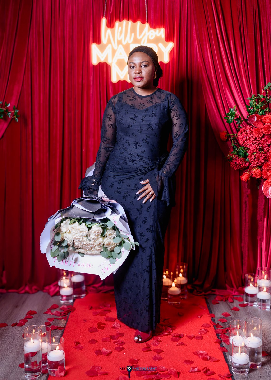 The bride posing with her bouquet in front of the Will You Marry Me neon and red rose backdrop