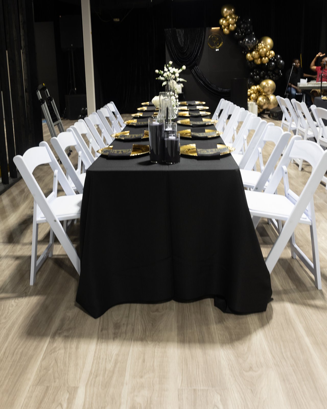 Long reception table with gold chargers and a black and gold balloon backdrop