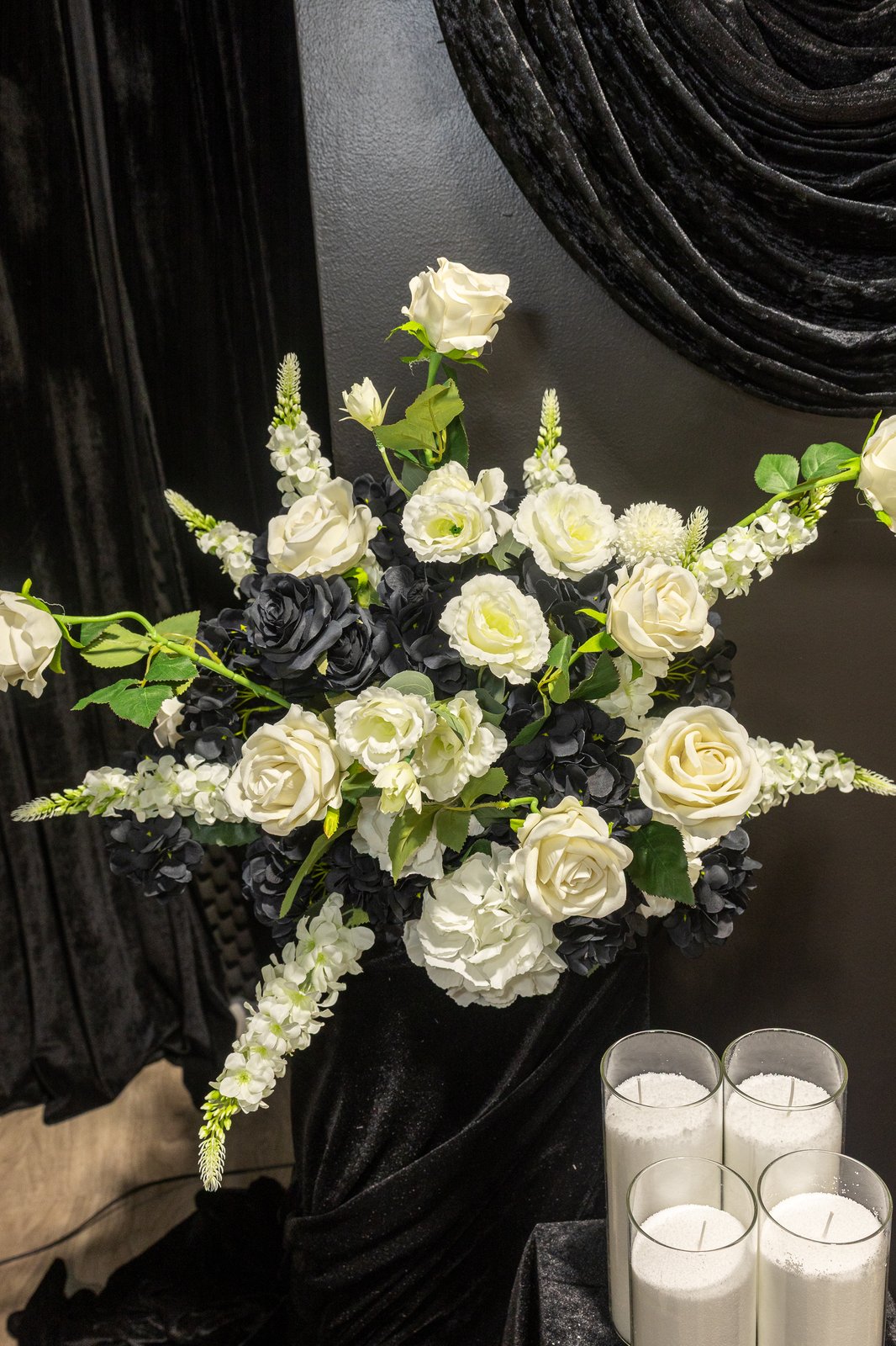 White rose and black floral arrangement against a black velvet drape