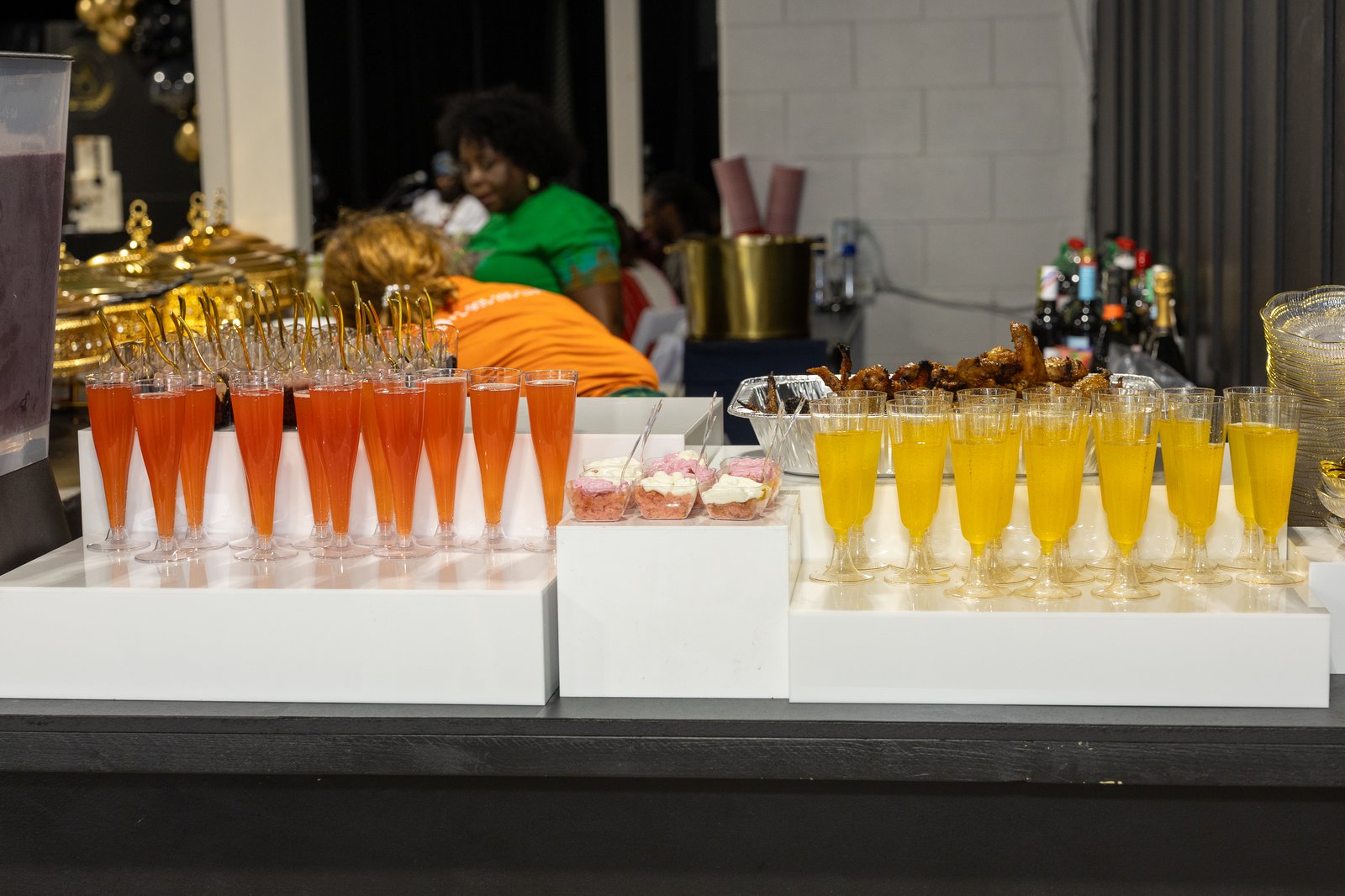 Mocktail drink station with rows of orange and gold beverage glasses on white pedestals