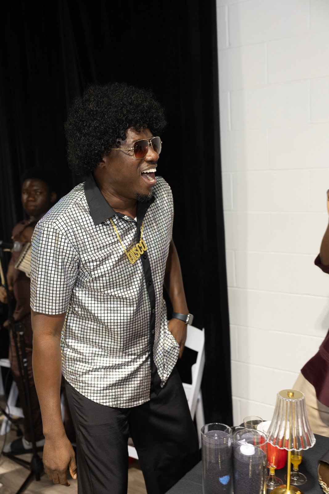 Guest in a silver disco shirt, afro wig, and gold Disco chain laughing