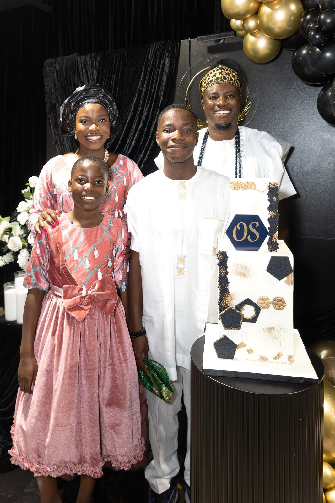 Family portrait beside the two-tier OS birthday cake, with the father in a gold crown and white agbada