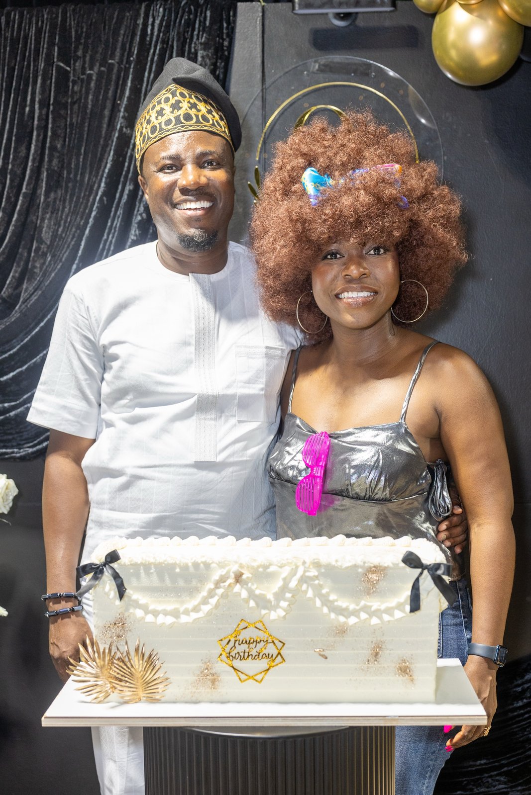 Couple posing with a sheet cake reading Happy Birthday