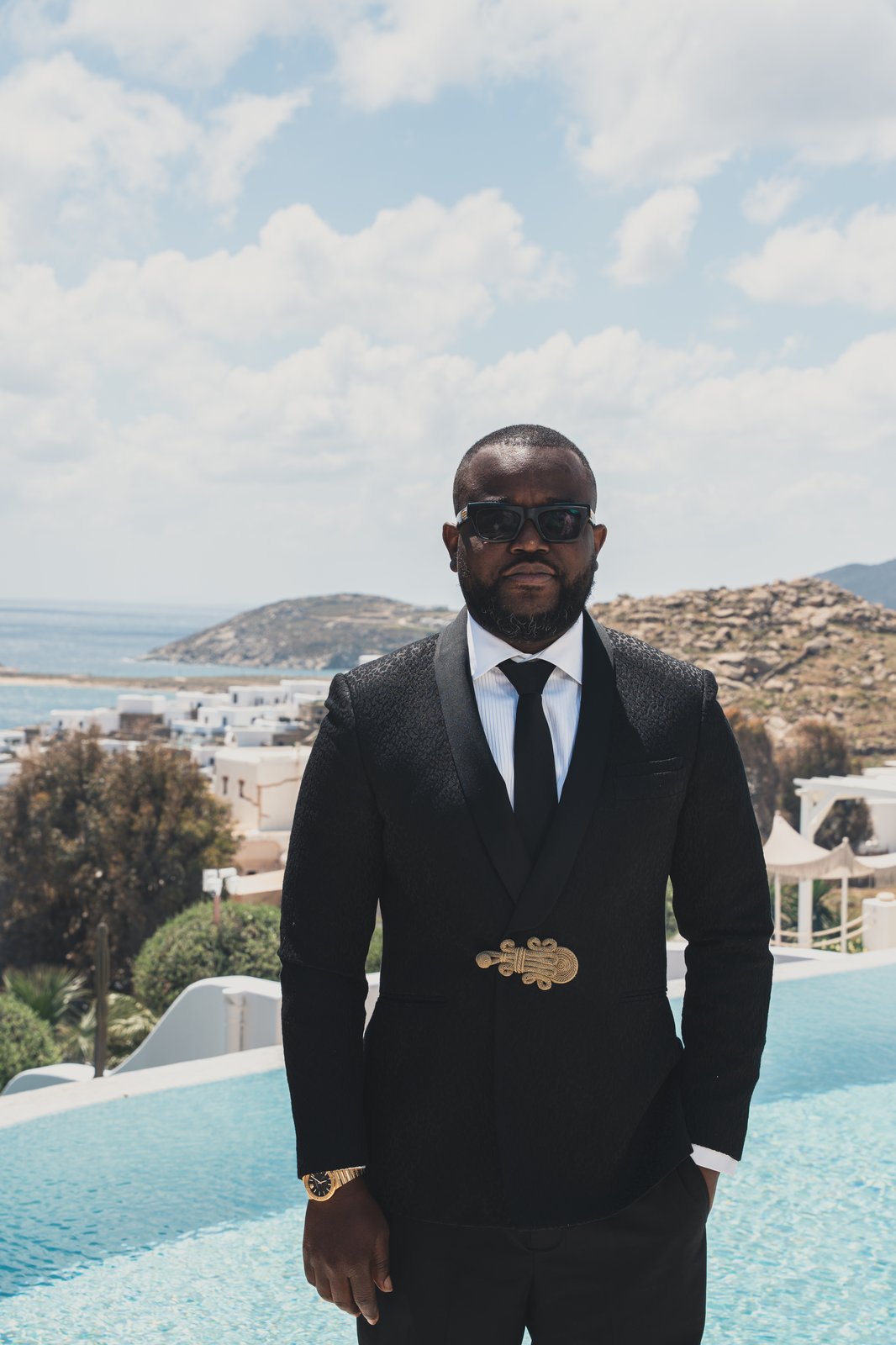 A groomsman in a dark suit standing poolside overlooking the sea before the ceremony