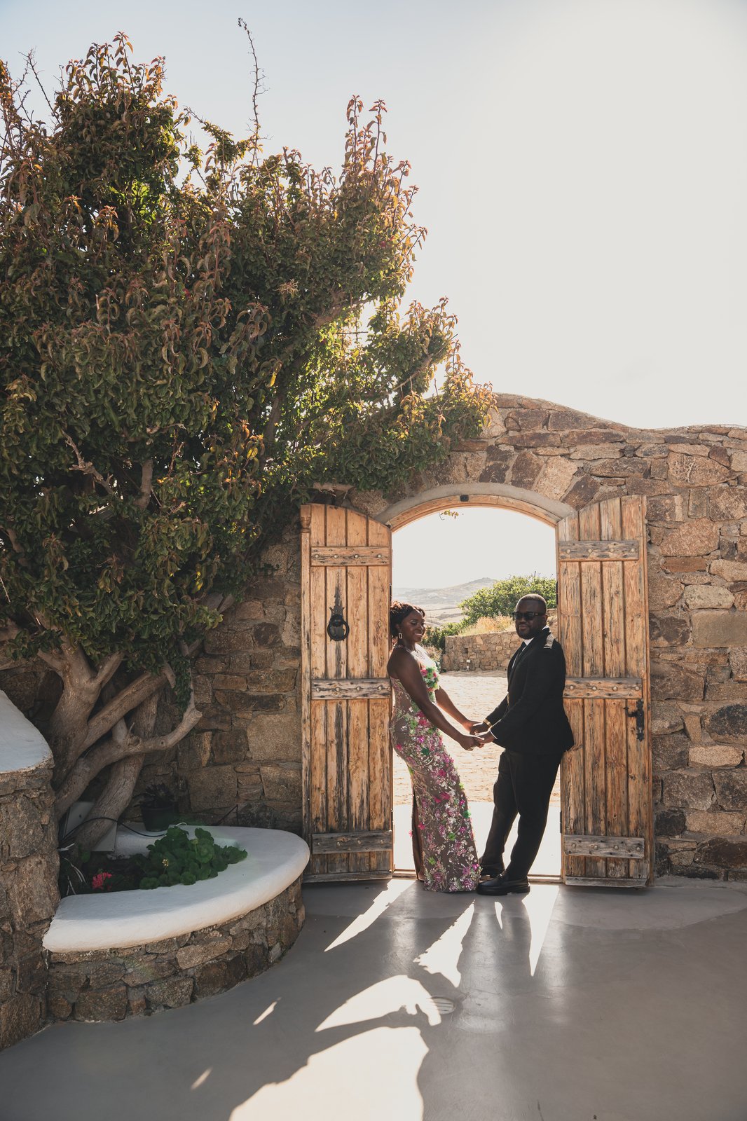 The couple walking hand in hand through a stone archway