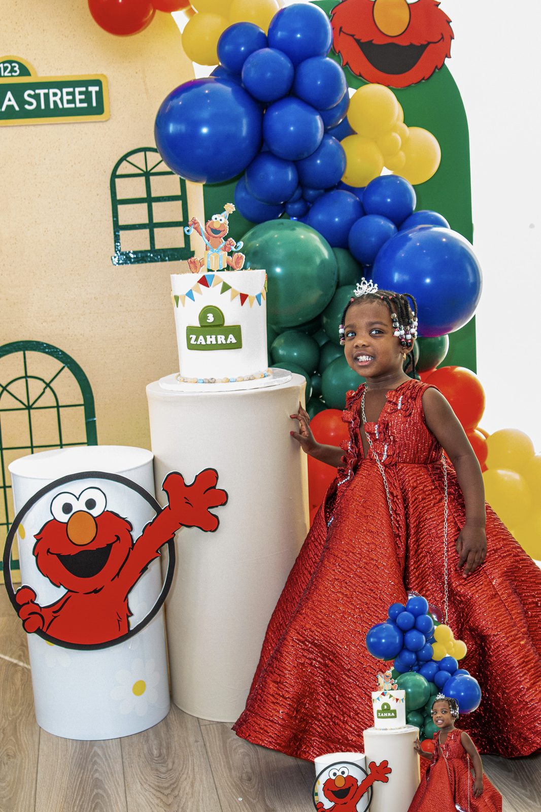 The birthday girl in a red gown beside her Zahra Street cake display