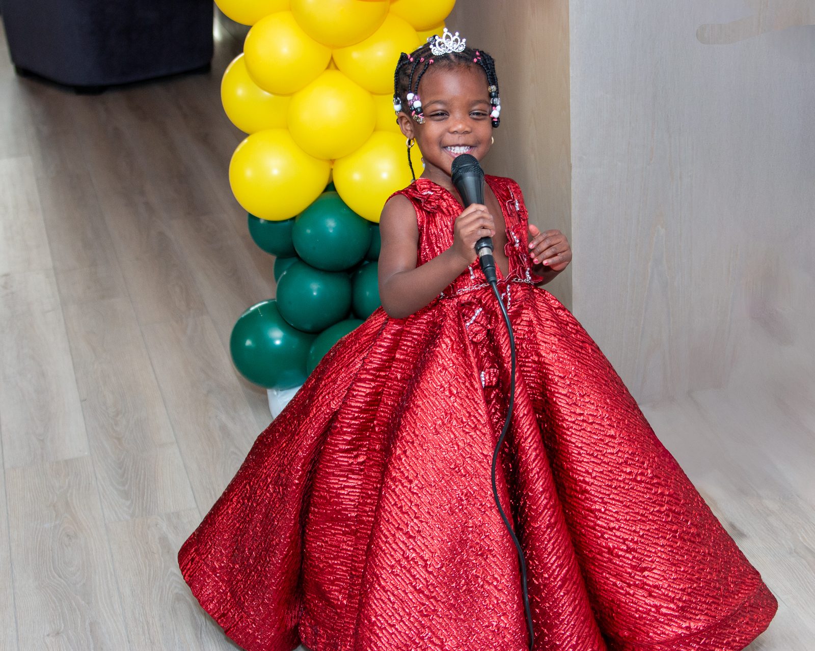 Zahra singing into a microphone in a red ball gown and tiara