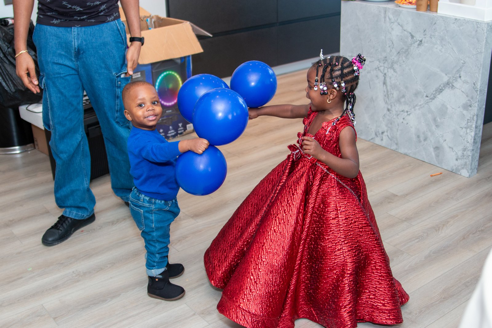 A guest and the birthday girl in a red dress surrounded by blue balloons