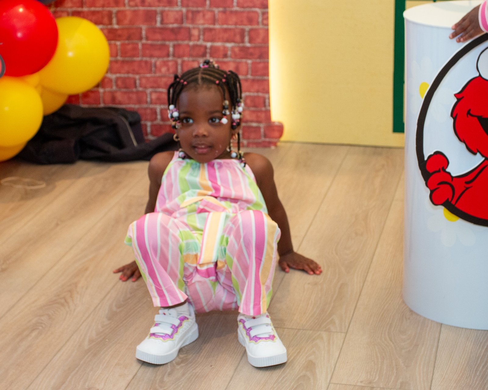The birthday girl crouching in a colorful striped outfit near the balloons
